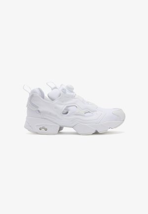 Białe sneakersy z teksturowaną, inżynieryjną siateczką. Posiadają wyraźne wycięcia, wyprofilowaną podeszwę i zaokrąglony kształt noska.