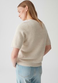 Lichtbeige korte mouwen trui met een zachte, pluizige textuur. Heeft een ronde halslijn en een ontspannen pasvorm, gecombineerd met lichte denim jeans.