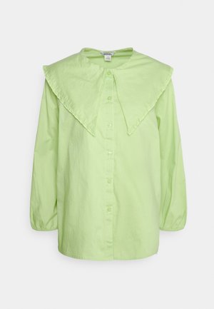 Camisa verde clara com colarinho largo e franzido. Botões à frente e mangas longas, ligeiramente bufantes, em tecido suave.