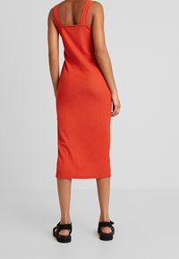 Punainen, muotoonompelu midi-mekko leveillä olkaimilla ja tekstuurilla. Siinä on sulava, yksinkertainen muotoilu, ja se ulottuu siististi polven alapuolelle.