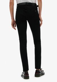 Jeans ajustados negros de mezclilla, con una cintura alta, dos bolsillos traseros y una textura suave. Combinados con zapatos negros brillantes.