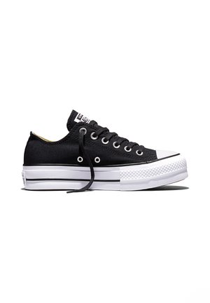Adidaș negru din pânză, cu talpă de cauciuc albă, ochiuri metalice și un șiret liber, arătat din lateral pe fundal alb.