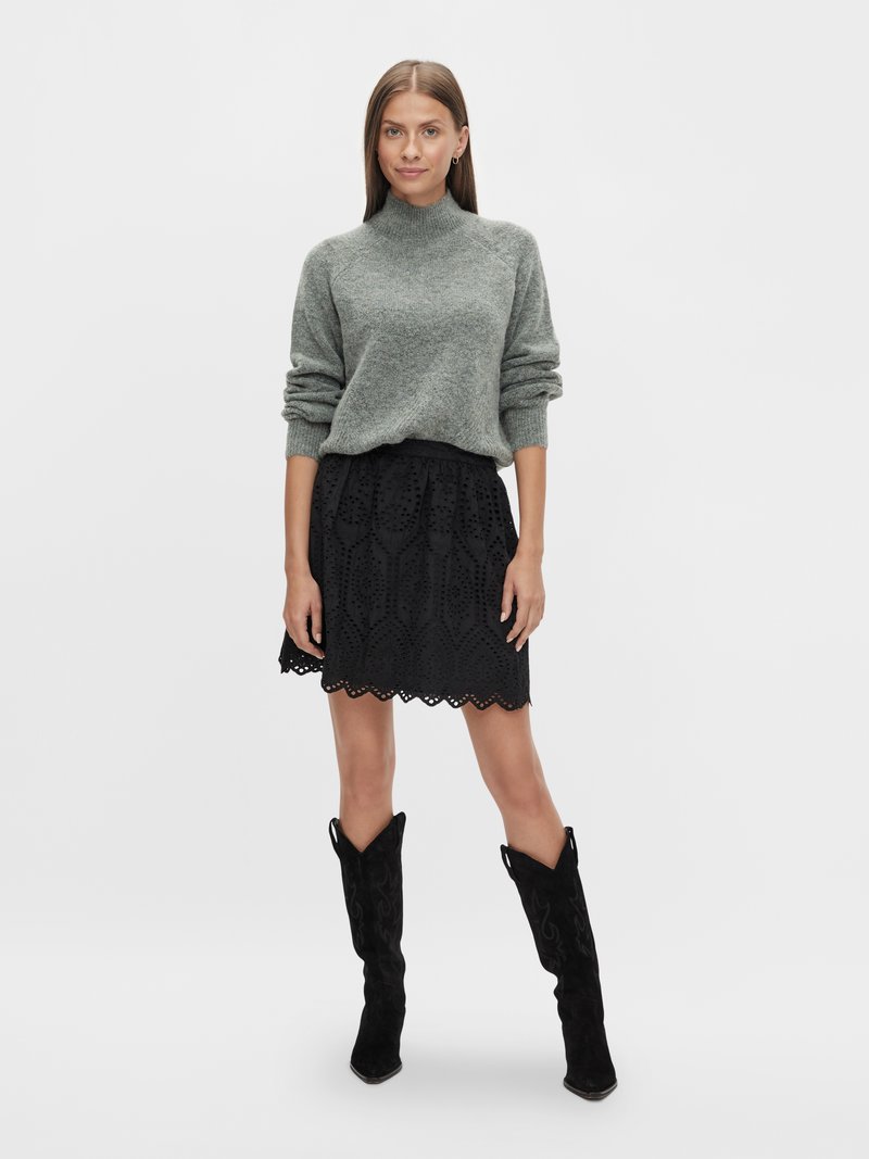 Grau gestrickter Rollkragenpullover, schwarzer bestickter Rock mit gewelltem Saum und schwarze Wildleder-Cowboystiefel mit spitzen Zehen.