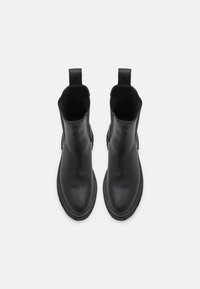 Mustat nahkaiset nilkkurit, joissa on sileäpintainen viimeistely, pyöreä kärki ja vetokieli yläosassa; hienovarainen tekstuuri ja joustava kumipohja.