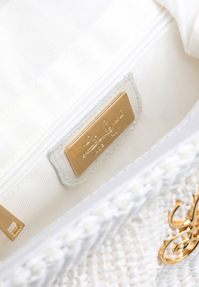 Intérieur d'un sac à main en tissu crème montrant une plaque de logo dorée gravée « Loewe Made in Italy » et un fermoir doré sur une doublure en tissu blanc.
