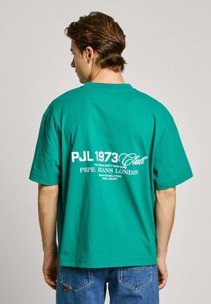 Green cotton t-shirt with a loose fit, featuring white printed text on the back, including "PJL 1973 Club" and brand details.