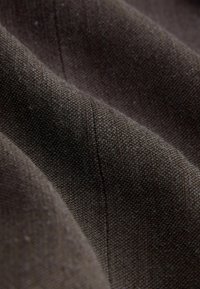 Dunkelbrauner Stoff mit einer strukturierten Webart, der feine Fäden und subtile Variationen aufweist. Die Oberfläche zeigt leichte Details und Falten.