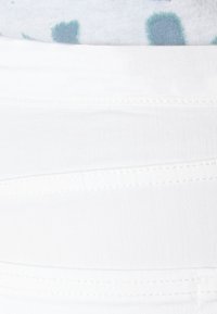 Pantalon en denim blanc avec détails de couture à l'avant et un haut de couleur claire partiellement visible au-dessus de la ceinture, orné de taches bleu-vert.