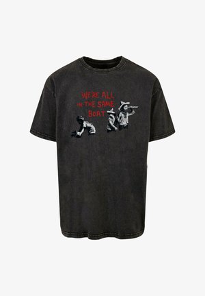 Black cotton t-shirt featuring the text "WE'RE ALL IN THE SAME BOAT" in red, with black and white graphic details of children.