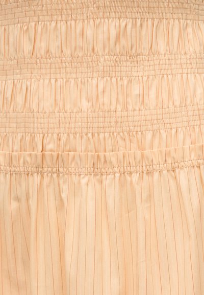 Ύφασμα σε ροδακινί απόχρωση με κάθετες λεπτές ρίγες, διαθέτοντας ραφή σμόκιν που συγκεντρώνει το ύφασμα και απαλή, ομαλή υφή. Οι λεπτομέρειες περιλαμβάνουν λεπτές, αντίθετες κλωστές.