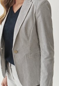 Gestreifter Blazer aus leichtem Stoff mit Reverskragen, einreihigem Knopfverschluss und einer Vordertasche. Farbe: Weiß mit Marineblauen Streifen.