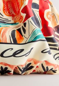Colorful fabric with abstract shapes, floral patterns, and black cursive text, draped to show folds and texture.