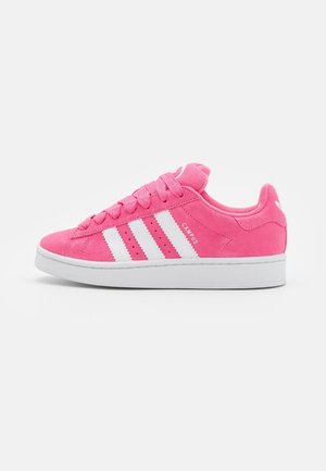 Roze suède Adidas Campus sneaker met witte strepen en witte zool, zijaanzicht op een effen witte achtergrond.