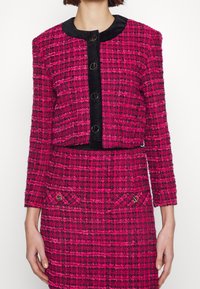 Rosa tweedjacka med svart mockakrage, kort design, guld rundade knappar och texturerad mönster, i kombination med en matchande kjol.