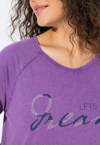 Fialové bavlněné tričko s kulatým výstřihem, na přední straně s potiskem "Let's Dream" v tmavě modré barvě a akcenty z kamínků.