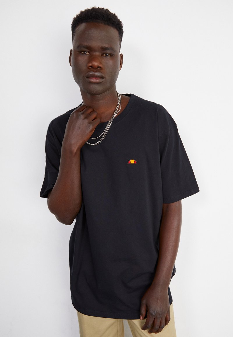 Schwarzes Baumwoll-T-Shirt mit kurzen Ärmeln und Rundhalsausschnitt. Mit einem kleinen gestickten Logo in Rot, Gelb und Orange auf der Brust.
