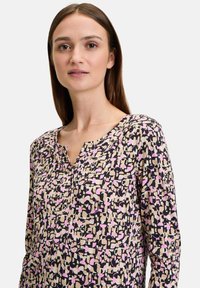 Bunte Bluse mit einem geometrischen Muster in Schwarz, Pink und Creme, mit V-Ausschnitt und langen Ärmeln. Weiche Stofftextur.