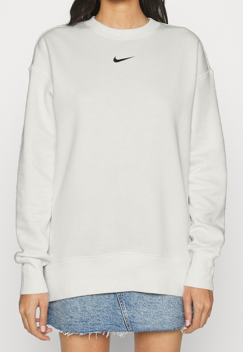 Sudadera blanca hecha de un tejido suave, con un logo negro de Nike en el pecho, puños y dobladillo acanalados, combinada con una falda de mezclilla.