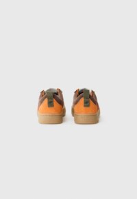 Pruunid ja oranžid nahast sneakersid, millel on tekstuurine pind, tan värvi kummitald ja konksuga tõmblukk kannas.