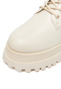 Kremowe skórzane buty z grubą, żłobioną podeszwą i okrągłym czubkiem. Posiadają dopasowane sznurowadła i minimalne detale szycia.