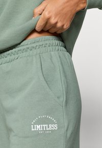 Zielone bawełniane dresy z elastycznym pasem, bocznymi kieszeniami i białym nadrukiem "LIMITLESS" na górnej części uda. Miękka faktura.