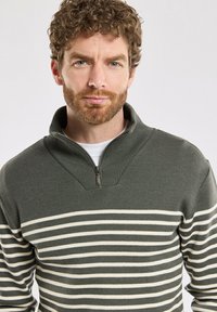 Lekki, oliwkowy sweter z zamkiem przy kołnierzu, z białymi poziomymi paskami. Strukturalny dziany materiał o luźnym kroju.
