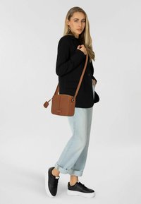 Blazer nero, jeans baggy azzurri chiari e sneakers nere con suole bianche. La borsa a tracolla marrone presenta una superficie texturizzata e una tracolla regolabile.