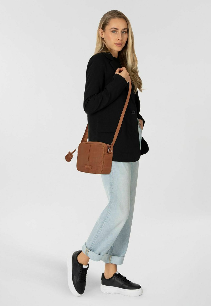 Blazer nero, jeans baggy azzurri chiari e sneakers nere con suole bianche. La borsa a tracolla marrone presenta una superficie texturizzata e una tracolla regolabile.