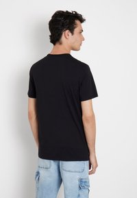 Camiseta negra de manga corta con un diseño clásico de cuello redondo. La tela parece suave y elástica. Se lleva con unos jeans de estilo cargo de color azul claro.