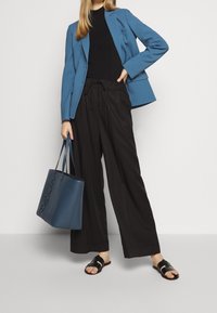 Blauwe blazer, zwarte ribbed top, zwarte wijde broek, zwarte sandalen, een blauwe tote bag met reliëflogo vasthoudend. Glad textuur, casual ontwerp.