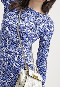 Blå klänning med blommönster och långa ärmar som är kombinerad med en liten vit handväska med en texturerad yta och detaljer i guld.