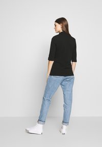 Svart tettsittende polo-skjorte med trekvart-ermer, parret med lyseblå rette jeans og hvite høyhælte sneakers.