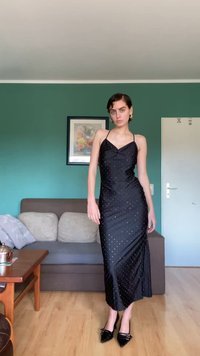 Juodas satino suknelė su prigludusia forma, plonomis petnešėlėmis ir lengvu drapiravimu. Dekoruota baltais taškeliais. Dėvima su juodais smailiais aukščiais.