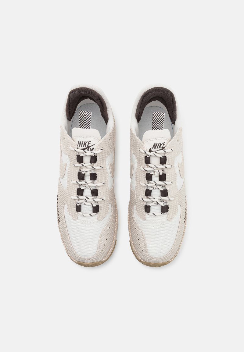 Baskets Nike Air avec une tige en mesh gris et blanc, des accents noirs, des lacets épais et une semelle en caoutchouc texturé, arborant un logo sur la languette.