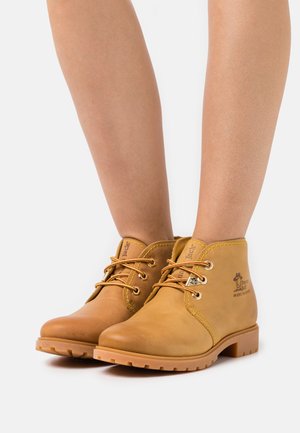 Botas de tobillo de cuero marrón con punta redonda, diseño de cordones y suela de goma. Presenta un logo en el lado y cordones en contraste.