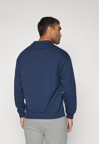 Hanorac bleumarin cu o croială lejeră, mâneci lungi, manșete și tiv din tricot. Textură moale, detalii minime și fără elemente grafice.