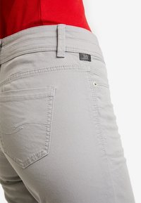 Vaaleanharmaat housut, joissa on teksturoitu pinta, taka-tasku ompeludetaljilla ja pieni merkkilappu vyötärönauhan lähellä.