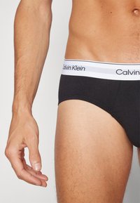 Fekete pamut alsónadrág fehér rugalmas derékrésszel, rajta a "Calvin Klein" logóval. Simán tapintású és testhezálló fazon.