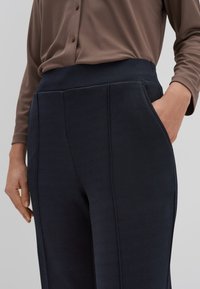 Navy blauwe op maat gemaakte broek van een gestructureerde stof, met een hoge tailleband en zijzakken. Gecombineerd met een bruin overhemd met knopen.