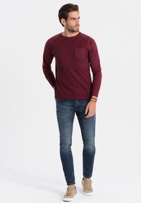 Burgundy pitkähihaisessa paidassa on ribbikuvio ja vasemmassa rinnassa tasku, joka on yhdistetty sinisiin skinny-farkkuihin ja vaaleisiin lenkkareihin. Yksinkertainen ja istuva muotoilu.
