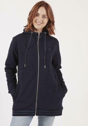 Veste à capuche navy en matériau doux avec une fermeture éclair, des poches avant et des accents rayés décoratifs aux poignets et à l'ourlet. Capuche réglable.