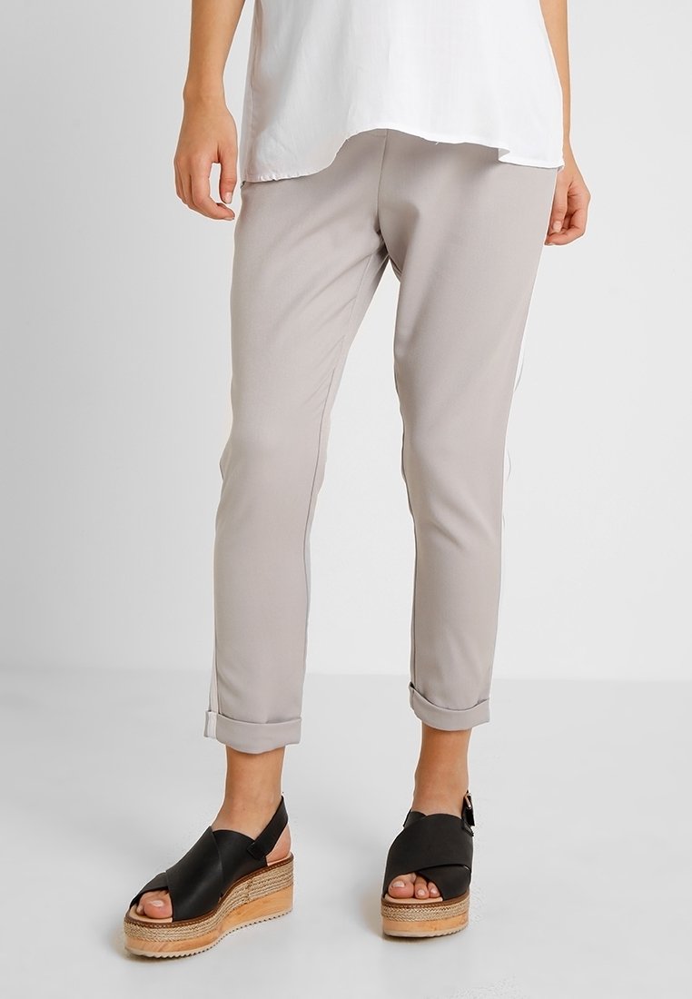 Pieds et jambes inférieures d'une personne portant un pantalon beige retroussé et des sandales à plateforme noires avec des semelles en bois.