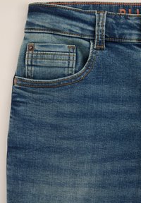 Jeans i ljusblåtvätt med en slät yta. Har en framficka med bronserad detaljer och kontrasterande orange sömmar.