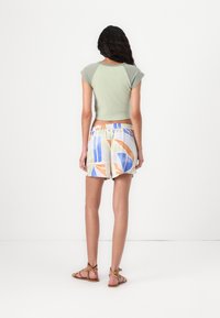 Top verde corto con maniche corte, abbinato a pantaloni corti colorati con fantasia in tessuto leggero. Sandali con cinghie color cuoio completano l'outfit.