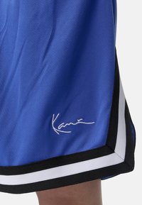 Shorts de sport bleus en tissu mesh, avec une taille élastique rayée noire et blanche et un détail de signature blanc à l'ourlet.