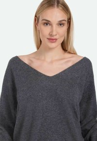 Maglione grigio, over-size, con scollo a V profondo, realizzato in un tessuto morbido e testurizzato. Presenta maniche lunghe e una vestibilità rilassata.
