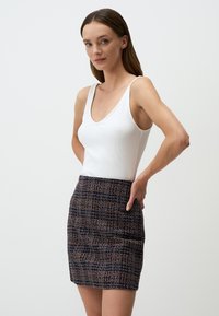Débardeur blanc à côtes avec un décolleté en V profond, associé à une mini-jupe en tissu tweed multicolore, avec un motif texturé et une taille élastique.