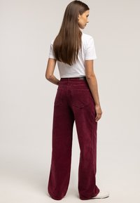 Bordowe spodnie szerokie z sztruksu o fakturowanej powierzchni. Posiadają tylne kieszenie i wysoki stan. Zestawione z gładkim białym t-shirtem.