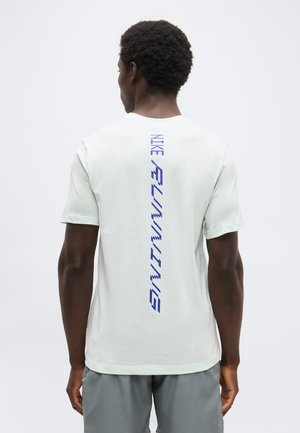 Άνδρας που φοράει λευκό αθλητικό T-shirt της Nike με μπλε κάθετη επιγραφή "NIKE RUNNING" στην πλάτη και γκρι σορτς, στέκεται μπροστά σε απλό φόντο.