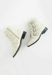 White leather ankle boots with three adjustable buckle straps and studded accents. Features a side zipper and a low black heel.